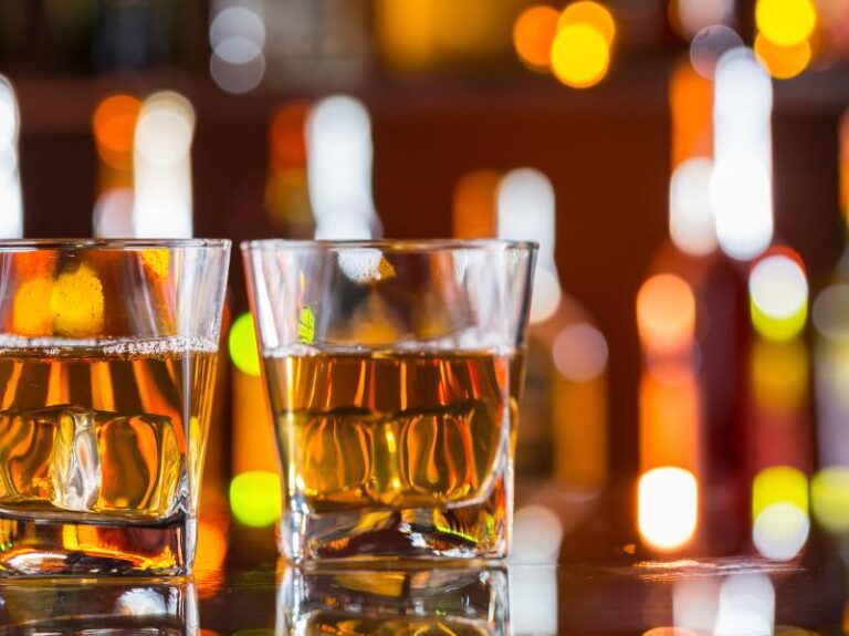 Two glasses of whiskey on the rocks on a reflective bar top