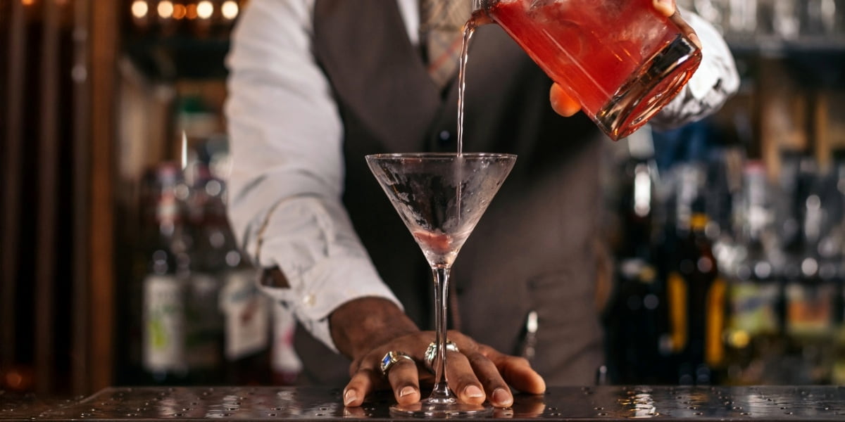 Bartender pouring a red cocktail into a martini glass, representing how to get a liquor license for serving mixed drinks in New York.