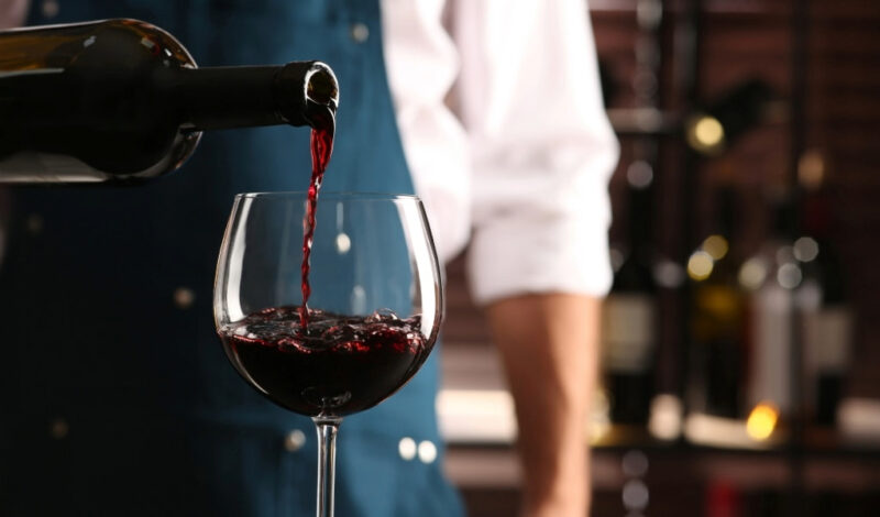 A bartender pouring red wine into a glass, illustrating types of liquor licenses needed to legally serve alcohol in New York.