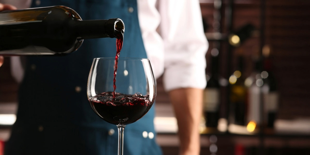 A bartender pouring red wine into a glass, illustrating types of liquor licenses needed to legally serve alcohol in New York.